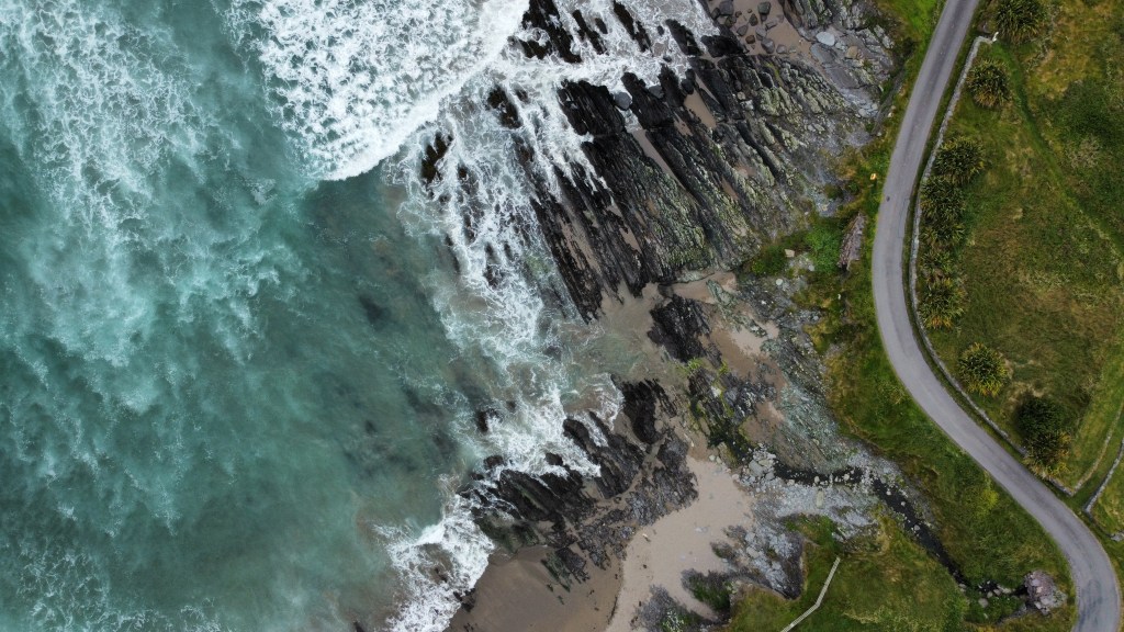 Drohnenaufnahme von brechenden Atlantikwellen mit weißer Gischt, Straße und Sandstrand in Irland (St. Finian's Bay)
