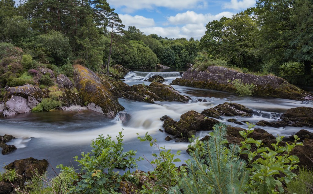Langzeitbelichtung von wilden Stromschnellen und kleinen Wasserfällen des Gearhameen River inmitten grüner Wälder im Killarney-Nationalpark am Ring of Kerry.