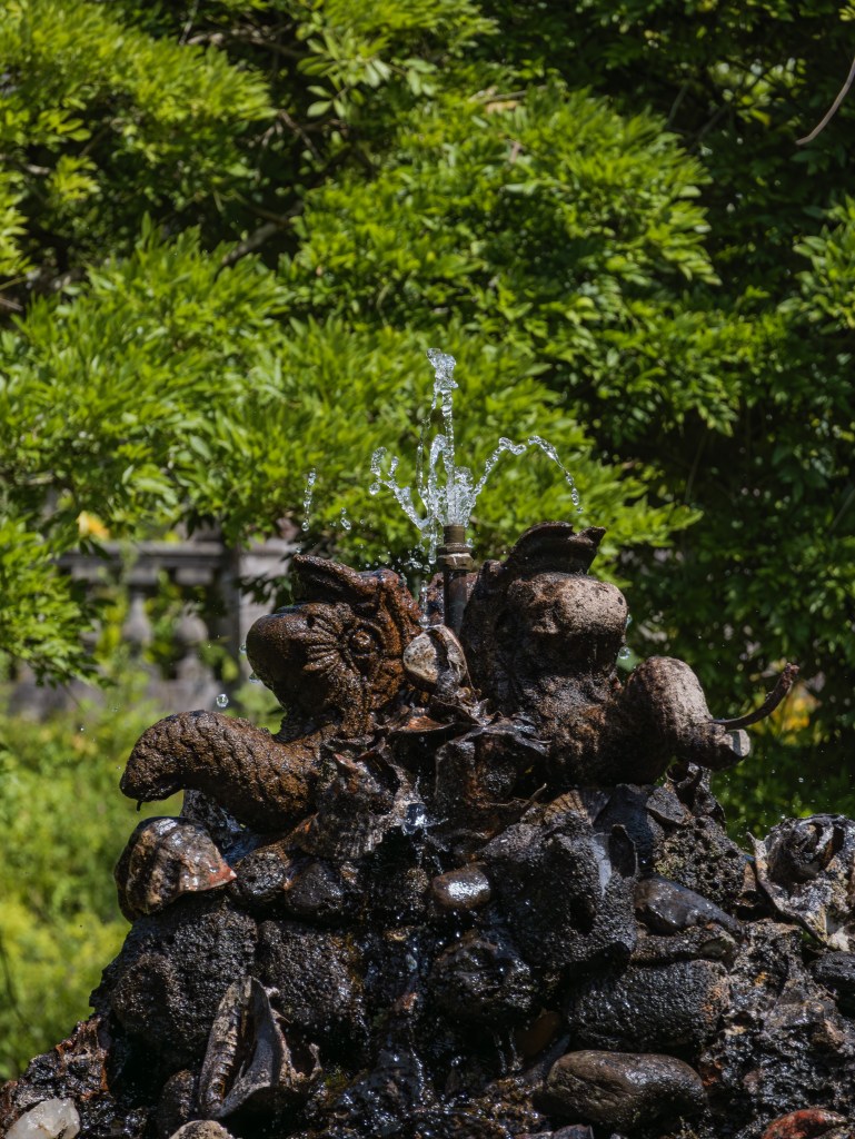 Nahaufnahme von einem historischen Springbrunnen mit steinernen Skulpturen und aufspritzenden Wassertropfen im Garten von Bantry House in Irland.